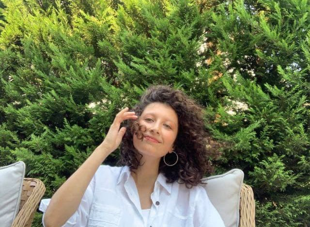 Geeske sitzt im Garten vor einer grünen Hecke