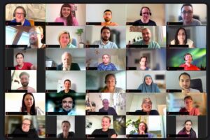 30 Personen in einer Videokonferenz, lächelnd und aufmerksam, beim wöchentlichen Kennenlernen-Gespräch.
