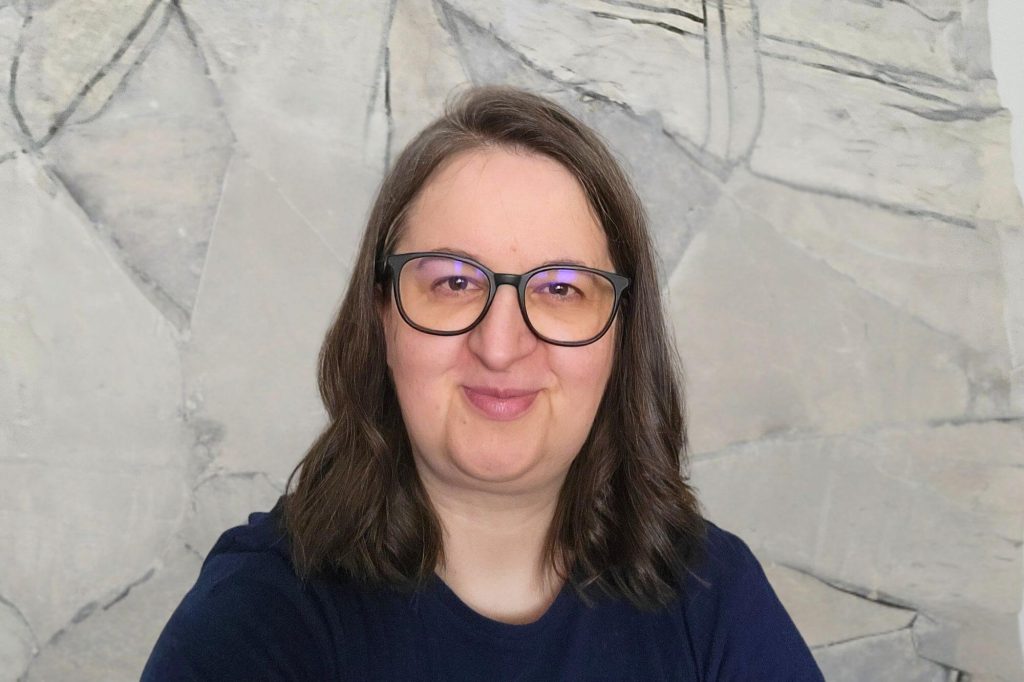 Annette mit langen dunkelblonden Haaren und Brille lächelt in die Kamera