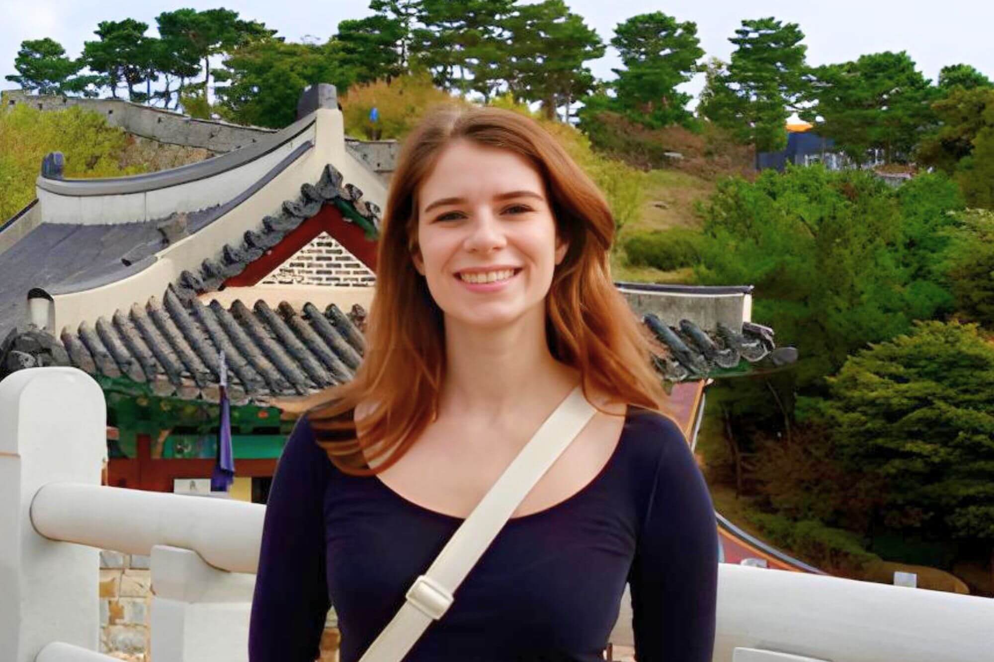 Eine junge Frau mit langen braunen Haaren steht draußen vor einer Pagode