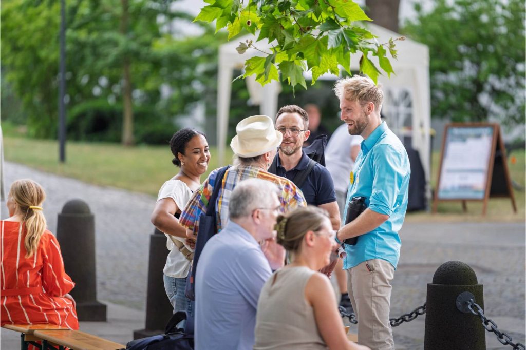 Oliver lachend im Gespräch mit einer Gruppe von Menschen